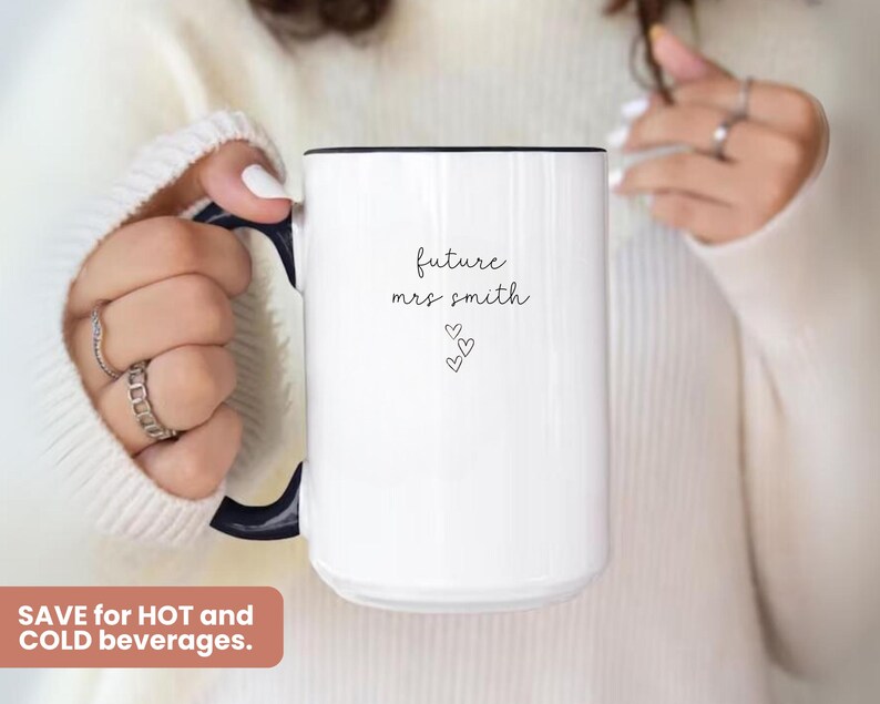 Pu&ograve; includere: Una tazza in ceramica bianca con un manico nero e il testo "future mrs smith" in scrittura nera. Tre piccoli cuori sono sotto il testo.