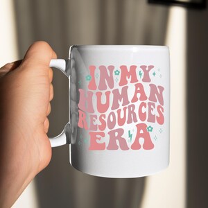 May include: White ceramic mug with a pink and blue design that says "In My Human Resources Era".