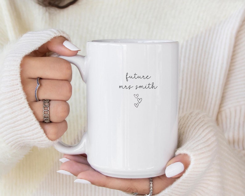 Pu&ograve; includere: Tazza in ceramica bianca con testo nero che recita "future mrs. smith" con tre piccoli cuori sotto il testo.