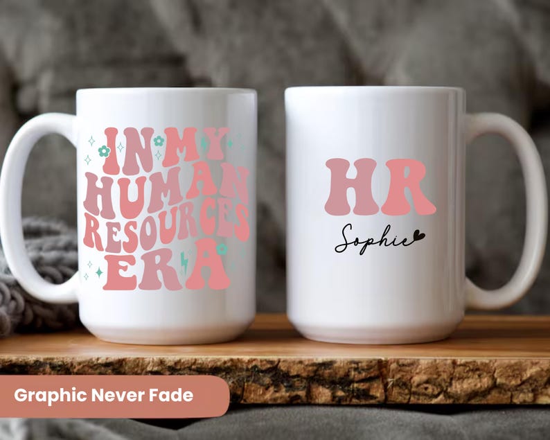 May include: Two white ceramic mugs with pink and green text. One mug says "In My Human Resources Era" and the other mug says "HR Sophie".