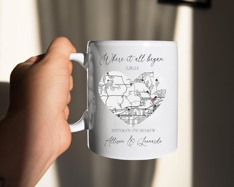 May include: White ceramic mug with a black and white map of a city in the shape of a heart. The text "Where it all began" is written above the map. The coordinates "39.17061N 76.36581W" and the names "Allison & Leonardo" are written below the map.