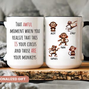 Op de afbeelding: Witte keramische mok met een zwart handvat en rand, met de tekst "THAT AWFUL MOMENT WHEN YOU REALIZE THAT THIS IS YOUR CIRCUS AND THOSE ARE YOUR MONKEYS." De mok toont ook cartoonapen met namen. Een "PERSONALIZED GIFT" label is zichtbaar.