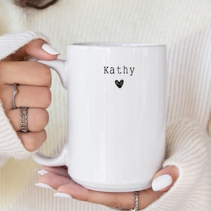 May include: White ceramic mug with a black heart and the name "Kathy" printed on it.