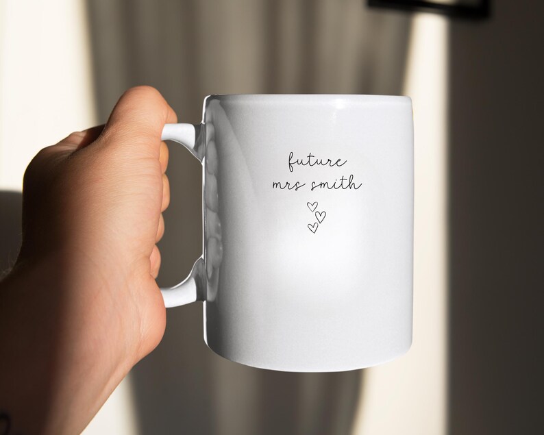 Pu&ograve; includere: Tazza in ceramica bianca con il testo "future mrs. smith" e tre piccoli cuori.