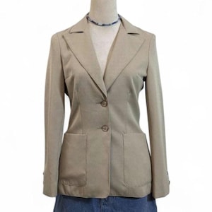 May include: A tan blazer with two front pockets and two buttons. The blazer has a notched collar and long sleeves. The blazer is displayed on a mannequin. A blue and white beaded necklace is around the mannequin's neck.