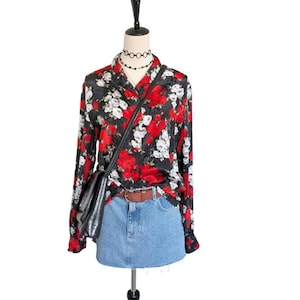 May include: A black floral print blouse with red and white roses, paired with a denim skirt and a black crossbody bag. The blouse has long sleeves and a collared neckline. A brown belt cinches the waist of the skirt.