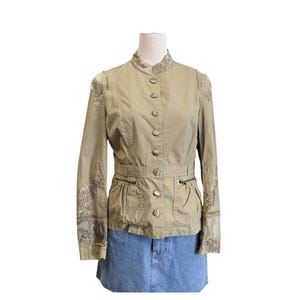 May include: A khaki-colored jacket with a mandarin collar and button-up front. The jacket features decorative embroidery on the shoulders and sleeves, along with two front pockets and a belted waist. The jacket is paired with a denim skirt.