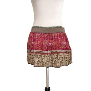 May include: A short skirt with a paisley pattern in shades of pink, orange, and yellow. The skirt has a brown waistband and a decorative border at the hem. The skirt is displayed on a mannequin.