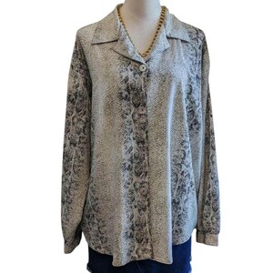 May include: A button-down shirt with a snakeskin pattern in shades of gray and black. The long-sleeved shirt has a collared neckline and is buttoned up the front. A gold-colored chain necklace is visible at the neckline.