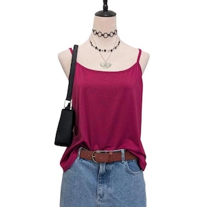 May include: A burgundy camisole top with spaghetti straps, paired with a denim skirt and a brown leather belt. A black shoulder bag hangs on the left side. The mannequin is also wearing layered necklaces.