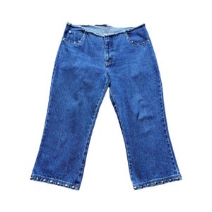 May include: Blue denim jeans with a cropped, flared leg. The jeans have silver-colored stud accents along the front pockets and the bottom hem. The waistline has a raw, unfinished edge.