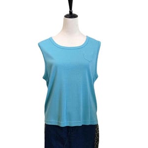 May include: A sleeveless, light blue top with a round neckline and a small pocket on the chest. The top is displayed on a mannequin and appears to be made of a soft, textured fabric. The bottom portion of the mannequin is wearing dark blue denim.