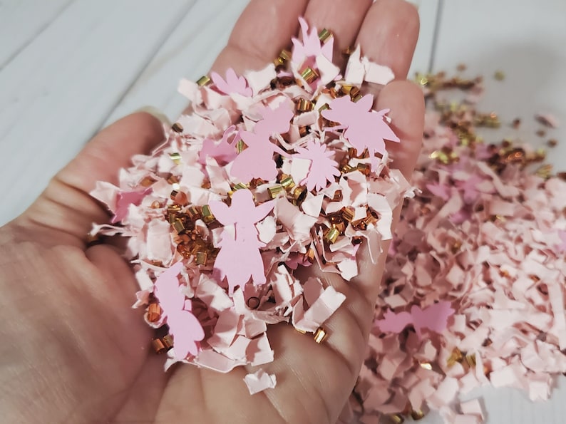 May include: Pink and gold confetti with fairy silhouettes. The confetti is made of paper and is perfect for adding a touch of whimsy to any celebration.