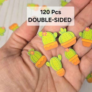 May include: Double-sided cactus-shaped stickers in various designs, including cacti in pots and with flowers. The stickers are primarily green, orange, and pink. The image includes the text "120 Pcs DOUBLE-SIDED".