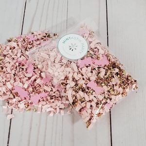 May include: Pink and gold confetti in a clear plastic bag. The confetti is made of paper and includes small pink unicorn shapes. The bag has a sticker that says "Mintastic Party".