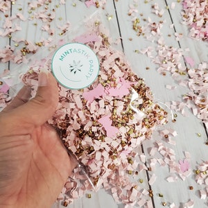 May include: A clear plastic bag filled with pink and gold confetti. The confetti is made of paper and includes small pieces of paper, stars, and butterflies. The bag has a sticker on it that says "Mintastik Party".