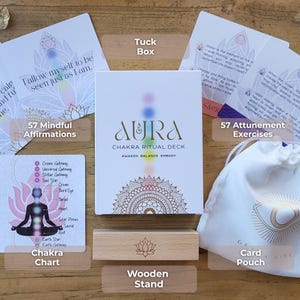 May include: Aura Chakra Ritual Deck set includes a tuck box, 57 mindful affirmations, a chakra chart, a wooden stand, 57 attunement exercises, and a card pouch. The deck's box features the text "Aura Chakra Ritual Deck" with a colorful design.