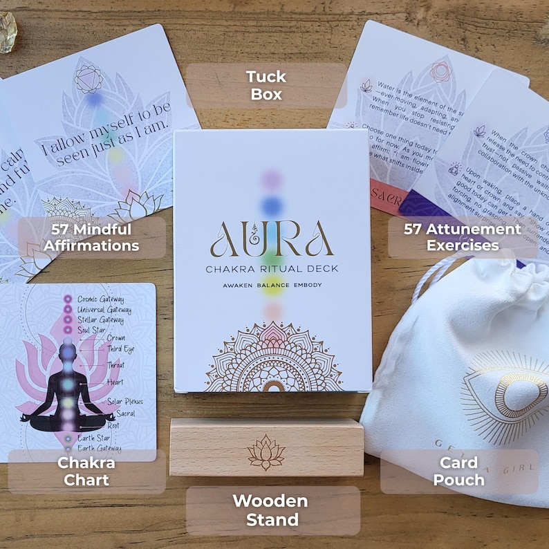 May include: Aura Chakra Ritual Deck set includes a tuck box, 57 mindful affirmations, a chakra chart, a wooden stand, 57 attunement exercises, and a card pouch. The deck's box features the text "Aura Chakra Ritual Deck" with a colorful design.