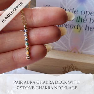 May include: A gold-colored necklace featuring seven colorful gemstones aligned vertically. The gemstones are in various colors, including red, orange, yellow, green, purple, and blue. The necklace is held in a hand, with the text "BUNDLE OFFER" in the upper left corner.