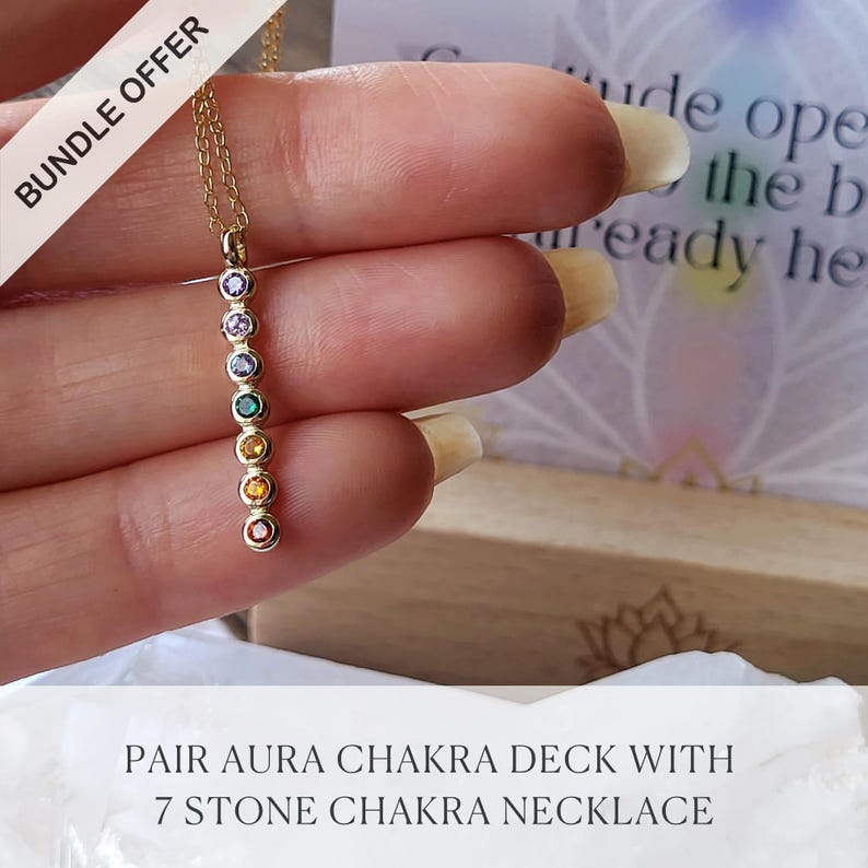 May include: A gold-colored necklace featuring seven colorful gemstones aligned vertically. The gemstones are in various colors, including red, orange, yellow, green, purple, and blue. The necklace is held in a hand, with the text "BUNDLE OFFER" in the upper left corner.