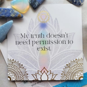 May include: A white card with the text "My truth doesn't need permission to exist." features a lotus flower design with gold accents and a rainbow gradient. Various blue and clear crystals are scattered around the card.