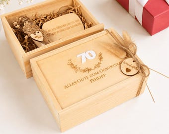 以下が含まれることがあります： 「70」という数字、「ALLES GUTE ZUM GEBURTSTAG」、「PHILIPP」という文字、そして花のリースが刻印されたスライド式蓋付きの明るい木製ギフトボックス。麻紐で「Wunscherfüller」と書かれた小さな木製タグが結び付けられています。
