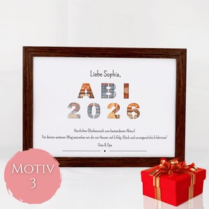 Pu&ograve; includere: Una cornice in legno marrone scuro contenente una stampa bianca con il testo "Liebe Sophia, ABI 2026" e un messaggio di congratulazioni in tedesco. Le lettere e i numeri presentano un motivo testurizzato. Una scatola regalo rossa con nastro oro.