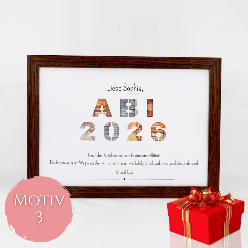 Pu&ograve; includere: Una cornice in legno marrone scuro contenente una stampa bianca con il testo "Liebe Sophia, ABI 2026" e un messaggio di congratulazioni in tedesco. Le lettere e i numeri presentano un motivo testurizzato. Una scatola regalo rossa con nastro oro.