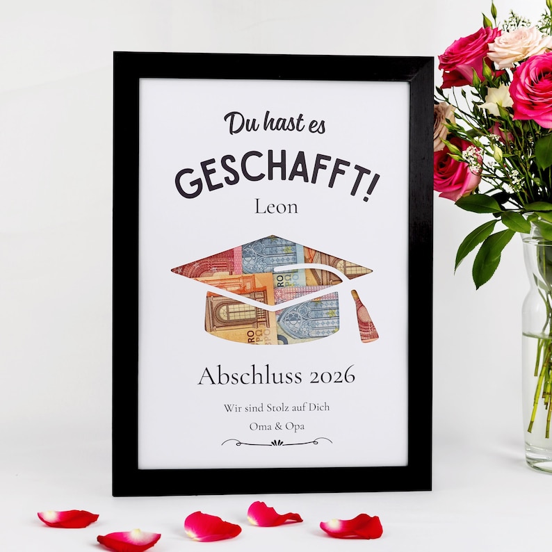 May include: Framed graduation art print with the German text "Du hast es GESCHAFFT!" (You did it!) and "Abschluss 2026" (Graduation 2026). The graduation cap is filled with Euro banknotes. Includes the name "Leon" and a message from "Oma & Opa".