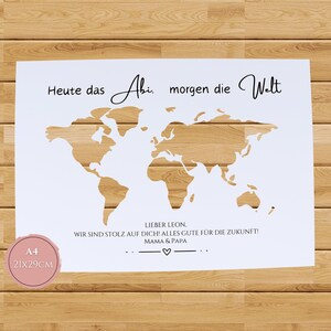 Pu&ograve; includere: Una stampa rettangolare bianca con un ritaglio di mappa del mondo che rivela un motivo a venature del legno. Il testo recita: Heute das Abi, morgen die Welt. Sotto: LIEBER LEON, WIR SIND STOLZ AUF DICH! ALLES GUTE F&Uuml;R DIE ZUKUNFT! MAMA & PAPA. &Egrave; visibile un'etichetta rosa A4 21x29cm.