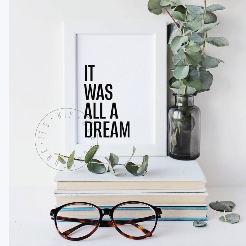 Puede incluir: Una impresi&oacute;n enmarcada en blanco con el texto "IT WAS ALL A DREAM" en letras negras. La impresi&oacute;n est&aacute; sobre una pila de libros con un par de gafas de montura marr&oacute;n delante de los libros. Una rama de vegetaci&oacute;n est&aacute; en un jarr&oacute;n de vidrio transparente a la derecha de la impresi&oacute;n.
