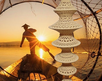 May include: A beige macrame hanging lamp with a tassel. The lamp is made of multiple layers of crocheted circles, creating a tiered effect. The lamp is hanging in front of a sunset scene with a fisherman in a boat.