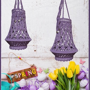 May include: Two purple macrame hanging planters with tassels, a wooden sign that says "SPRING", a bouquet of yellow tulips, and purple and white speckled Easter eggs on a whitewashed wood background.