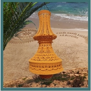 May include: A large, yellow crocheted lampshade hangs from a chain against a backdrop of a sandy beach with the words "PRAIA MARIA LUISA ALBUFEIRA" written in the sand.