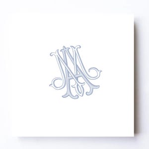 May include: A square white card featuring a centred, light blue monogram of the intertwined letters M and A. The letters are rendered in a decorative, calligraphic script with elegant flourishes and a subtle shadow effect for depth.