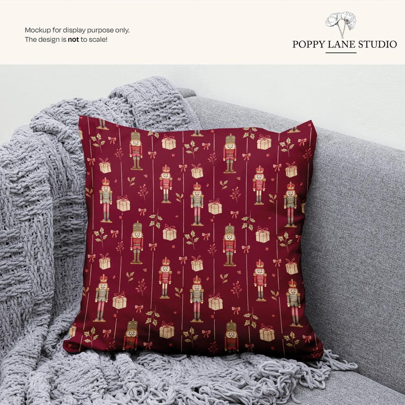 May include: A square decorative pillow with a festive pattern. The pillow features a deep red background with a repeating design of nutcrackers, gift boxes, and sprigs in shades of gold and cream. The pillow is displayed on a gray sofa with a knitted throw.