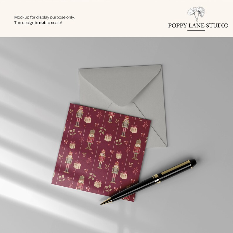 May include: A greeting card with a burgundy background featuring a pattern of nutcrackers and gift boxes, with a matching envelope and a black and gold pen. The text "POPPY LANE STUDIO" is visible.