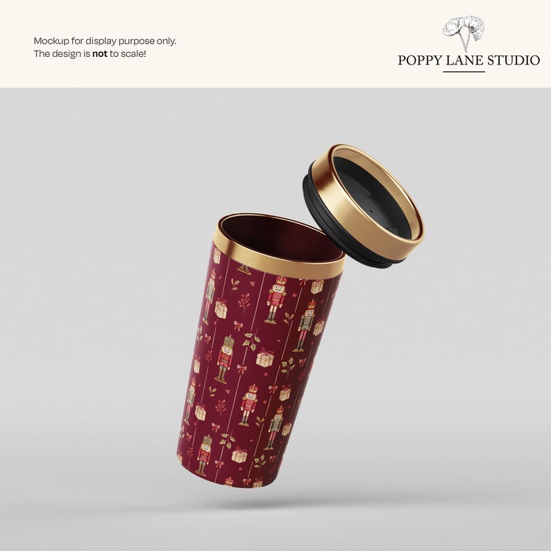 May include: A maroon travel mug with a gold rim and lid, featuring a repeating pattern of nutcrackers and gift boxes. The lid is black with a gold rim. The text "POPPY LANE STUDIO" is visible.