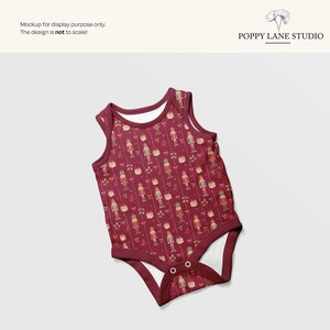 May include: A burgundy baby onesie with a repeating pattern of nutcrackers, gifts, and floral elements. The onesie has a round neckline and snap closures. The text "Mockup for display purpose only. The design is not to scale!" is visible.