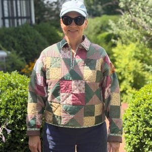 May include: A long-sleeve pullover jacket constructed from a patchwork quilt featuring a variety of square and triangular fabric patterns in shades of forest green, burgundy, cream, and tan, finished with a collar and a partial front zipper closure.