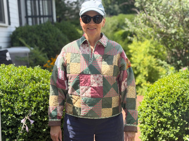 May include: A long-sleeve pullover jacket constructed from a patchwork quilt featuring a variety of square and triangular fabric patterns in shades of forest green, burgundy, cream, and tan, finished with a collar and a partial front zipper closure.
