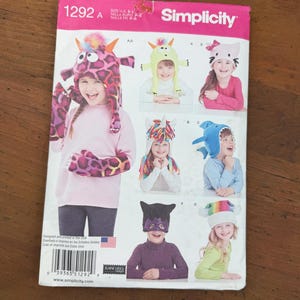 May include: Simplicity sewing pattern 1292 A featuring children's costume hats. The pattern includes designs for a giraffe, cat, unicorn, shark, and other whimsical characters. The pattern is printed in the USA.