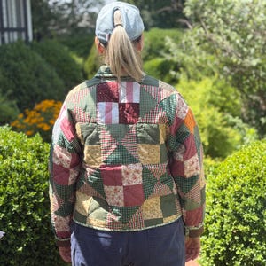May include: A quilted jacket featuring a patchwork design of various fabric squares in shades of green, red, yellow, and white. The garment has a collared neckline, long sleeves, and a button-up front, showcasing a mix of floral and checkered patterns.