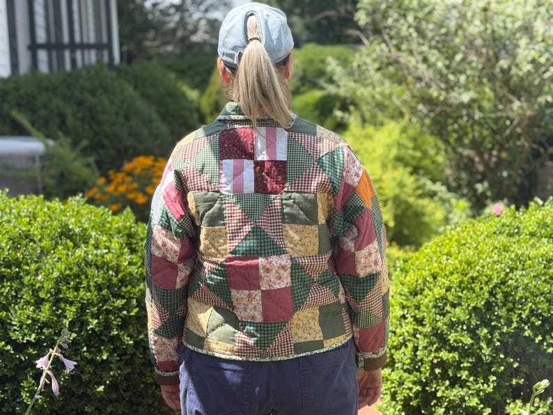 May include: A quilted jacket featuring a patchwork design of various fabric squares in shades of green, red, yellow, and white. The garment has a collared neckline, long sleeves, and a button-up front, showcasing a mix of floral and checkered patterns.