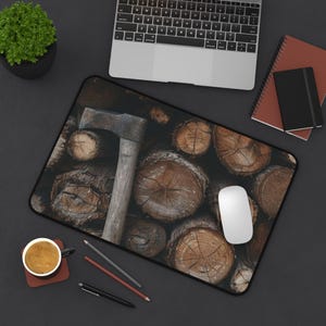 May include: A computer mousepad featuring a rustic design of stacked logs and an axe. The mousepad has a black border and is surrounded by a laptop, notebooks, a coffee cup, and writing utensils.