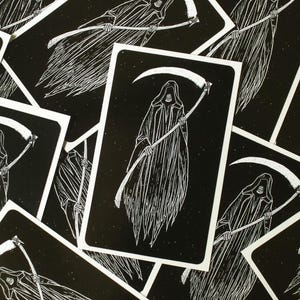 May include: A set of black and white tarot cards featuring a grim reaper with a scythe. The cards have a vintage, woodcut style.