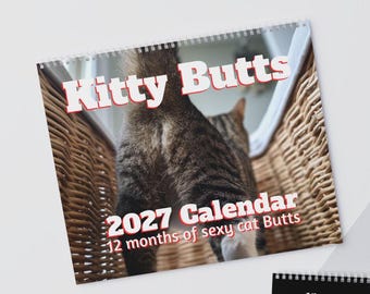 May include: A 2027 wall calendar titled Kitty Butts, featuring a photograph of a tabby cat standing in a wicker basket. The text reads Kitty Butts, 2027 Calendar, and 12 months of sexy cat Butts in white letters with a red outline on the cover.
