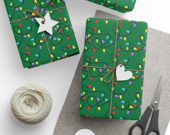May include: Three wrapped gifts with green paper featuring a colorful string light pattern. Each package is tied with twine and a white paper tag. A ball of twine, scissors, and blank tags are also visible.