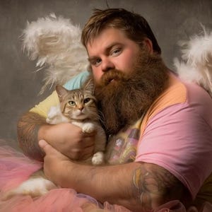 May include: A person with a long beard and tattoos, wearing a pink and yellow shirt, and a pink tutu, holding a cat. The person has white feathered angel wings. The cat is light brown and white.