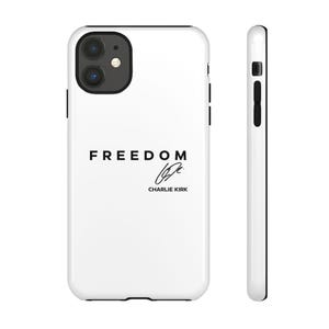 May include: White iPhone case with black trim. The case features the word "FREEDOM" in a bold, black font, along with a signature and the name "CHARLIE KIRK" in a smaller font below. The case is shown from the front and side.